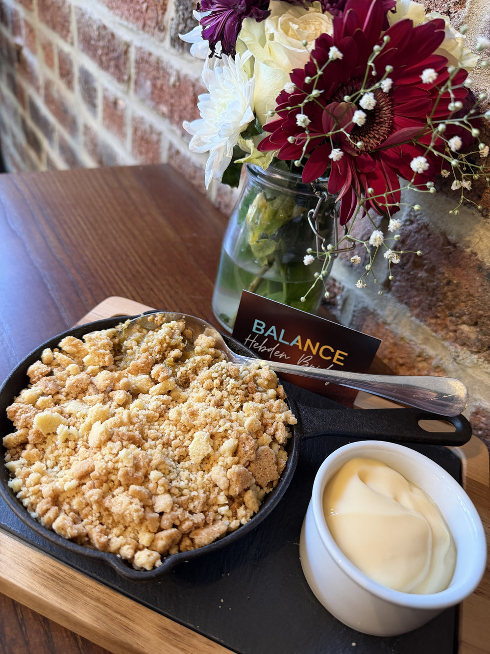 A crumble served with cream beside flowers inside BALANCE